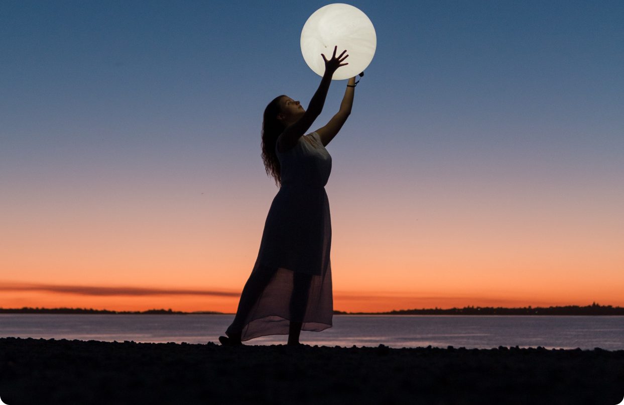 Woman in sheer dress reaching upwards to embrace the moon.